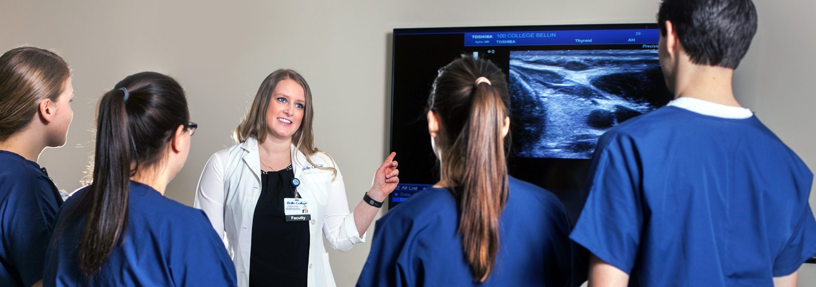 Sonography instructor showing students a patient scan on a large screen TV.